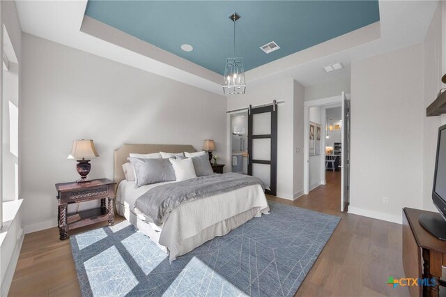 105 Monterey Oak Trl, Georgetown, TX 78628 - bedroom featuring a tray ceiling, a barn door, dark wood-style floors, and baseboards