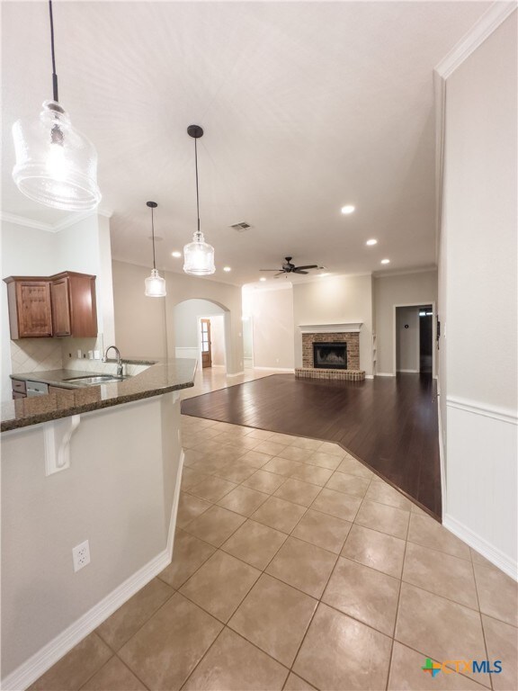 kitchen with a brick fireplace, ornamental molding, light hardwood / wood-style flooring, decorative light fixtures, and dark stone countertops