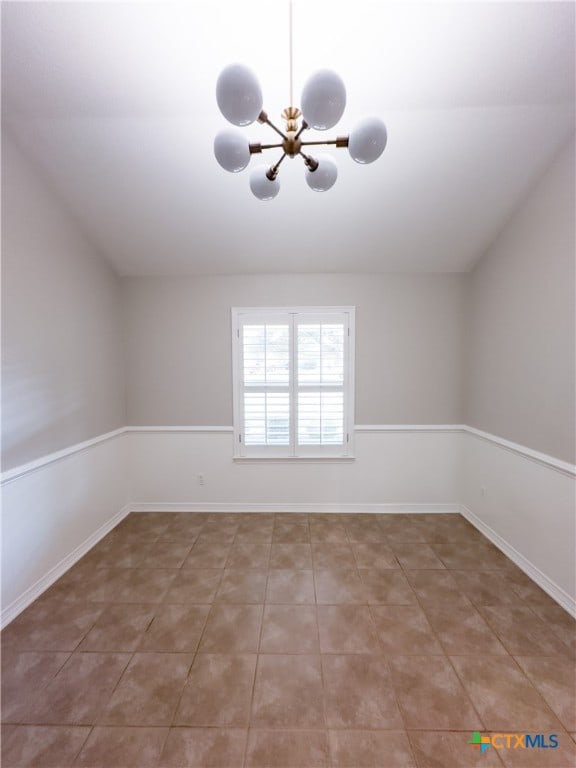 tiled empty room with vaulted ceiling and an inviting chandelier