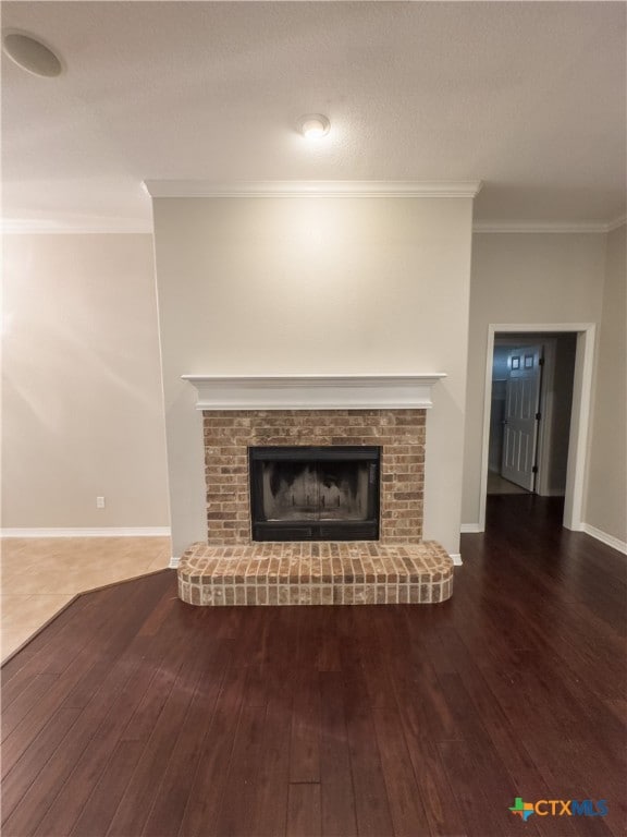 unfurnished living room featuring a brick fireplace, dark wood-type flooring, and crown molding