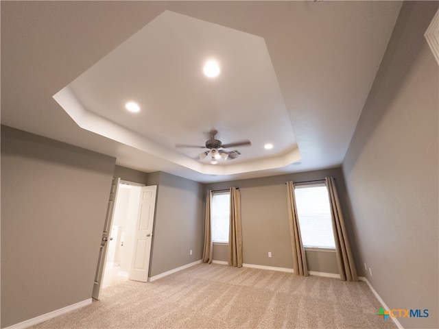 spare room featuring light carpet, ceiling fan, and a tray ceiling