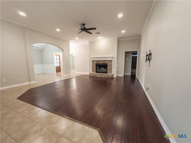 unfurnished living room with a brick fireplace, ceiling fan, light hardwood / wood-style flooring, and crown molding