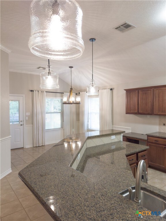 kitchen featuring sink, light tile patterned floors, crown molding, a notable chandelier, and vaulted ceiling