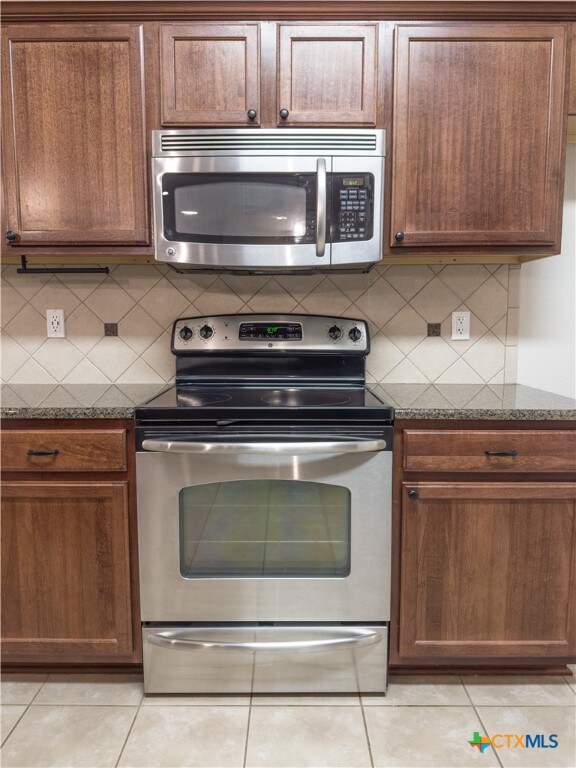 kitchen featuring dark stone counters, backsplash, appliances with stainless steel finishes, and light tile patterned floors