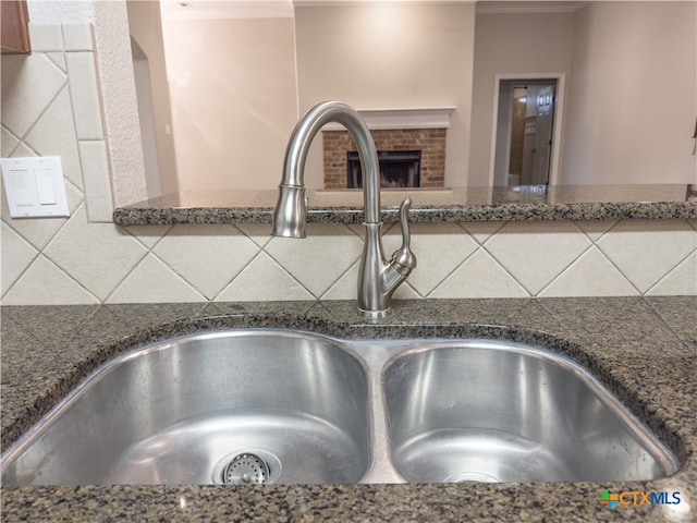 room details featuring dark stone countertops, backsplash, sink, and a brick fireplace