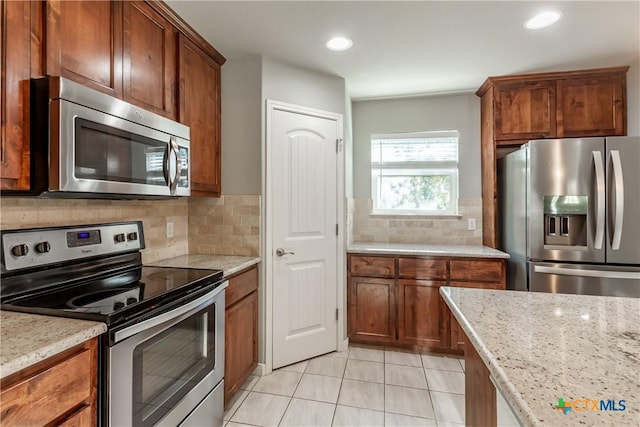 kitchen with light tile patterned flooring, stainless steel appliances, decorative backsplash, and light stone counters