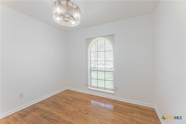 empty room with an inviting chandelier, baseboards, and hardwood / wood-style floors