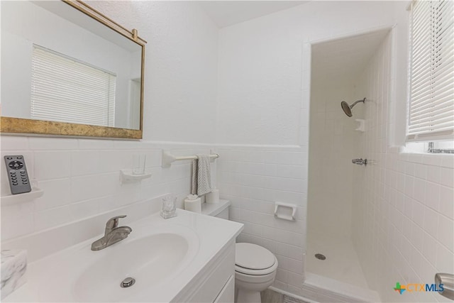 full bath with toilet, a tile shower, tile walls, wainscoting, and vanity