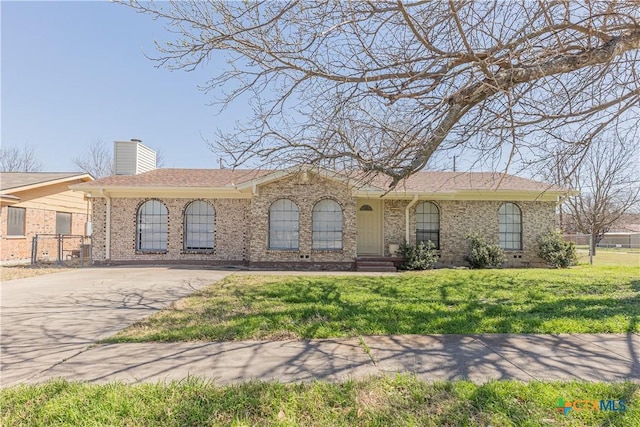 ranch-style home with brick siding, driveway, a chimney, and a front yard