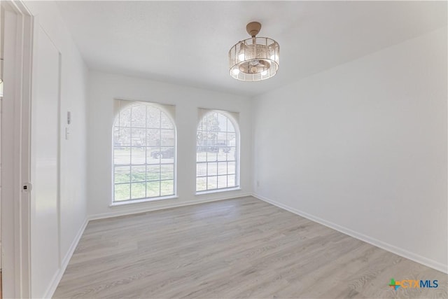 spare room with light wood finished floors, a healthy amount of sunlight, and baseboards