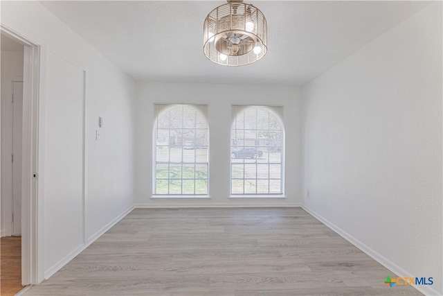 spare room featuring a notable chandelier, light wood-type flooring, and baseboards