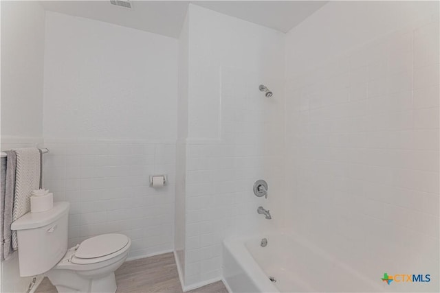 full bath featuring washtub / shower combination, a wainscoted wall, wood finished floors, tile walls, and toilet