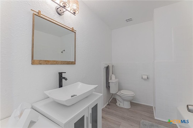 full bathroom with visible vents, toilet, wood finished floors, tile walls, and vanity