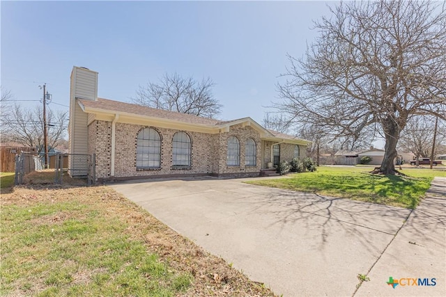 ranch-style home featuring a front yard, fence, driveway, a chimney, and brick siding