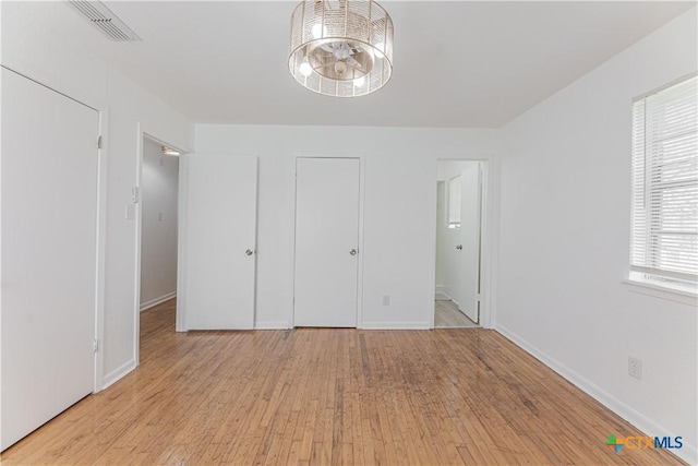 unfurnished bedroom featuring a notable chandelier, visible vents, baseboards, and wood finished floors