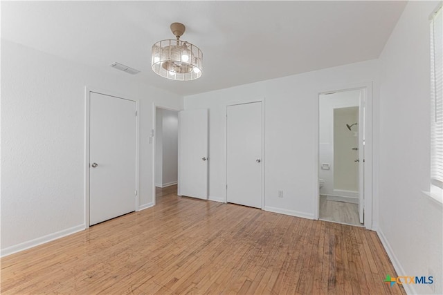 unfurnished bedroom with visible vents, baseboards, ensuite bath, and wood finished floors