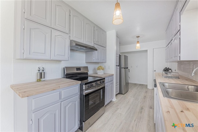 kitchen featuring butcher block countertops, under cabinet range hood, a sink, appliances with stainless steel finishes, and decorative backsplash