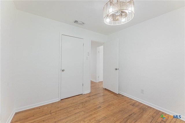 empty room featuring a notable chandelier, visible vents, light wood-style flooring, and baseboards