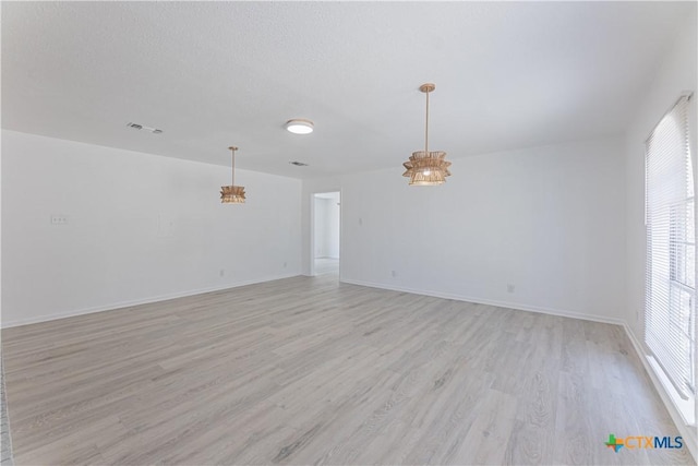 spare room with visible vents, baseboards, light wood-type flooring, a notable chandelier, and a textured ceiling