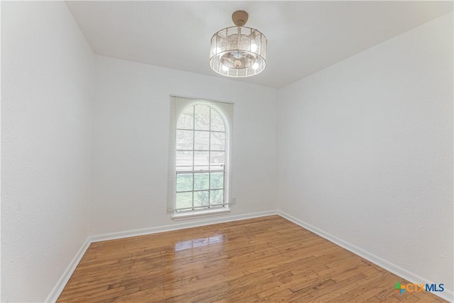 empty room with light wood-style flooring, a notable chandelier, and baseboards