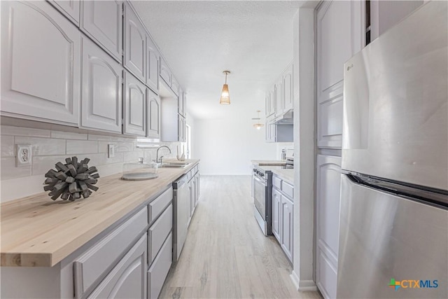 kitchen featuring light wood finished floors, backsplash, under cabinet range hood, stainless steel appliances, and a sink