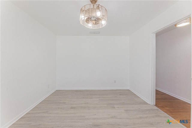 unfurnished room featuring a notable chandelier, baseboards, and light wood-style floors