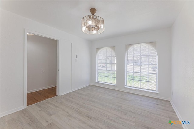 empty room with baseboards, an inviting chandelier, and wood finished floors