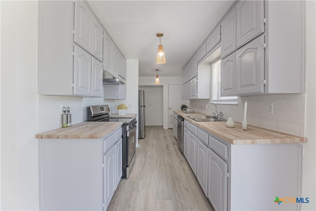 kitchen featuring a sink, under cabinet range hood, stainless steel appliances, light wood finished floors, and decorative backsplash