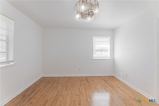 spare room featuring light wood-type flooring, baseboards, and an inviting chandelier