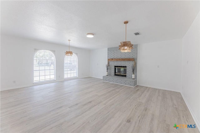 unfurnished living room featuring baseboards, visible vents, light wood finished floors, a fireplace, and a textured ceiling