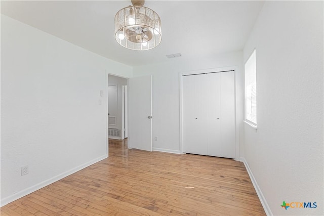 unfurnished bedroom with visible vents, baseboards, a notable chandelier, and light wood finished floors