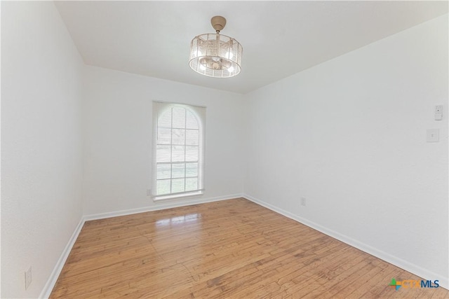 spare room with a notable chandelier, baseboards, and light wood-style floors