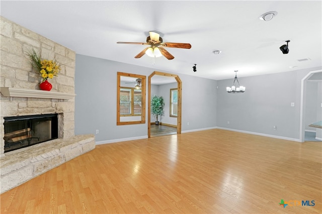 unfurnished living room with ceiling fan with notable chandelier, light hardwood / wood-style floors, and a stone fireplace