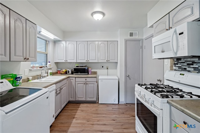 kitchen featuring separate washer and dryer, light hardwood / wood-style floors, sink, tasteful backsplash, and white appliances