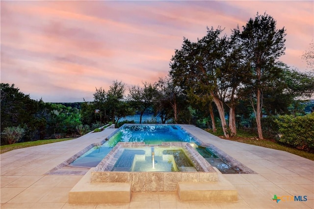 pool at dusk featuring an in ground hot tub