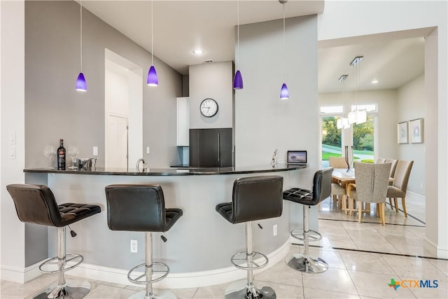 kitchen with decorative light fixtures, stainless steel fridge, a kitchen bar, and kitchen peninsula