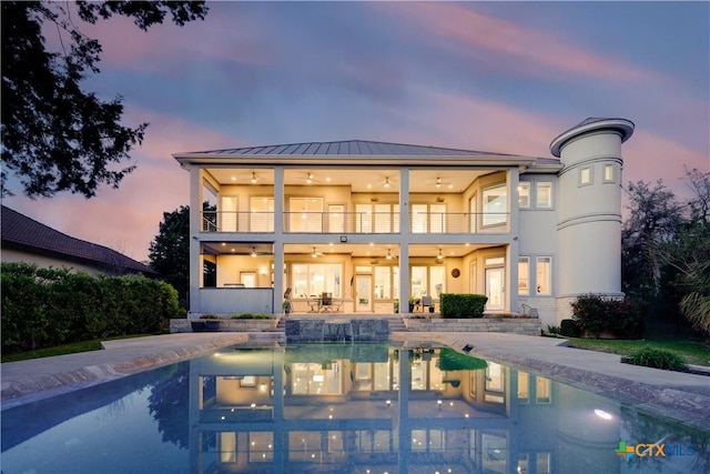 back house at dusk with a patio area, ceiling fan, and a balcony