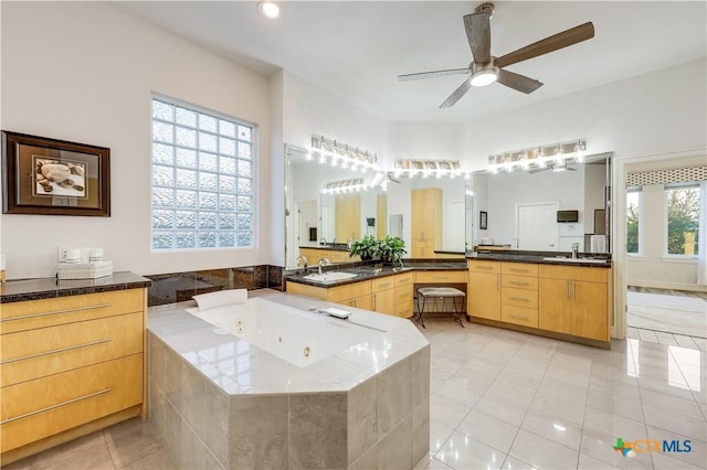 bathroom featuring ceiling fan, a healthy amount of sunlight, tile patterned flooring, a relaxing tiled tub, and vanity