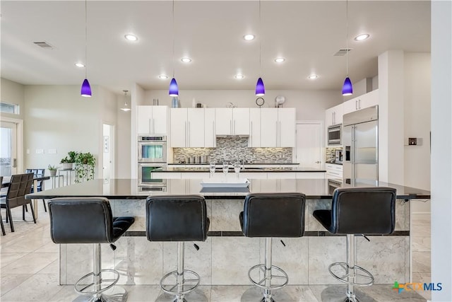 kitchen with white cabinets, pendant lighting, built in appliances, and a kitchen island with sink