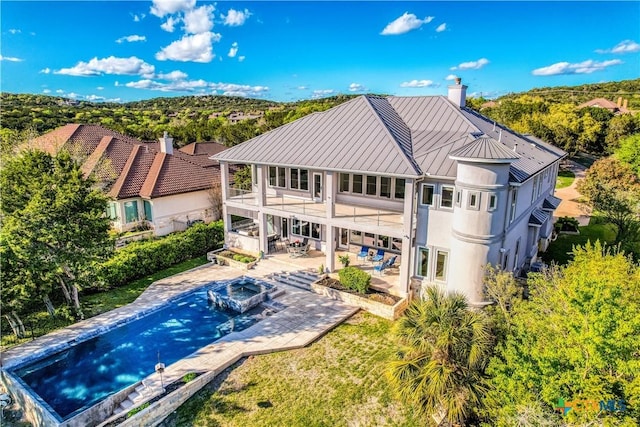 back of property with a swimming pool with hot tub, a balcony, and a patio area