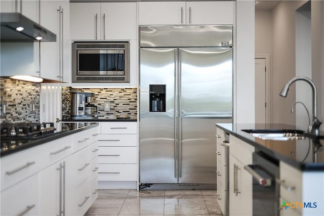 kitchen with built in appliances, decorative backsplash, white cabinetry, and sink