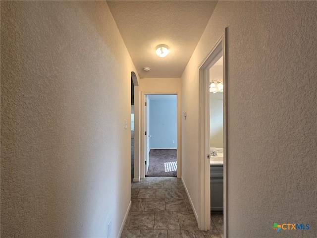 hallway with a textured ceiling, baseboards, arched walkways, and a textured wall