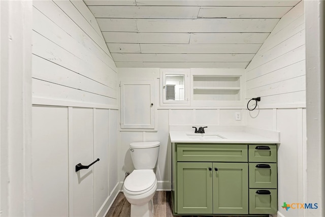 bathroom featuring hardwood / wood-style flooring, vanity, wooden walls, toilet, and vaulted ceiling