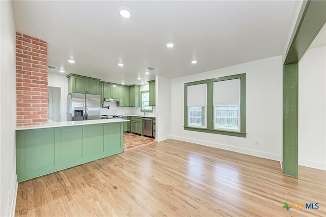 kitchen with backsplash, appliances with stainless steel finishes, green cabinetry, sink, and light hardwood / wood-style floors