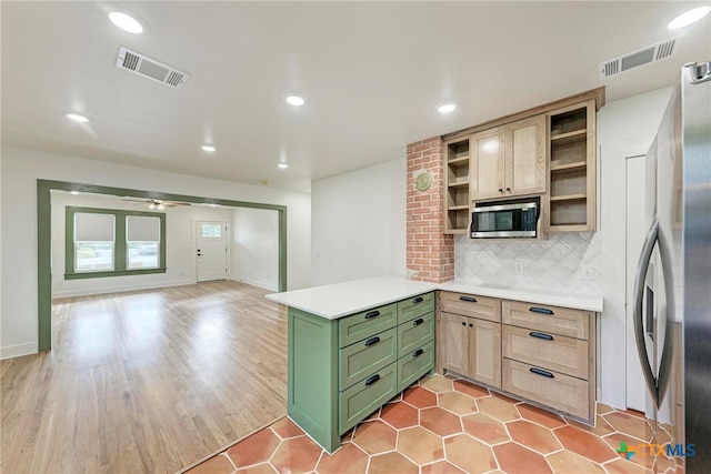 kitchen with light hardwood / wood-style floors, green cabinets, appliances with stainless steel finishes, tasteful backsplash, and light brown cabinets