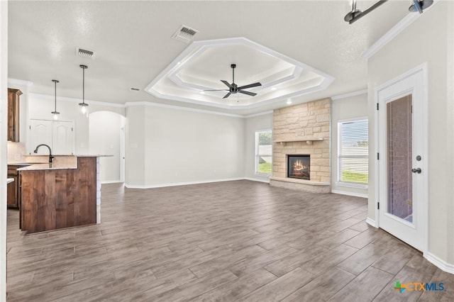 unfurnished living room with sink, ceiling fan, ornamental molding, a fireplace, and a tray ceiling