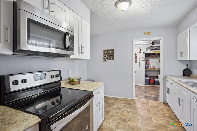 138 Antrim Dr, San Antonio, TX 78218 - kitchen featuring appliances with stainless steel finishes, light countertops, white cabinetry, a textured ceiling, and baseboards