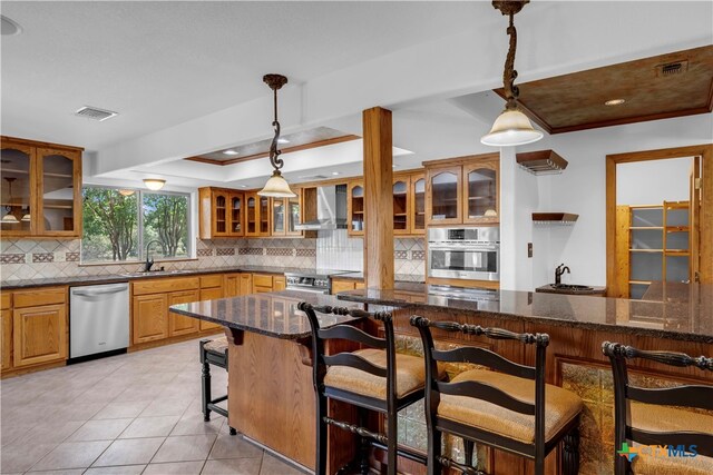 kitchen featuring a kitchen bar, pendant lighting, appliances with stainless steel finishes, and wall chimney range hood