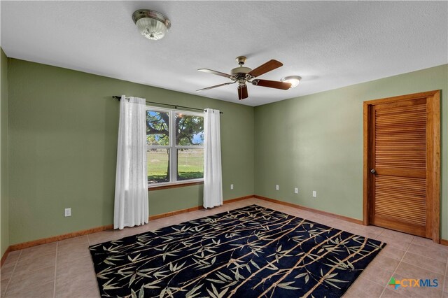 unfurnished room featuring a textured ceiling, ceiling fan, and light tile patterned flooring