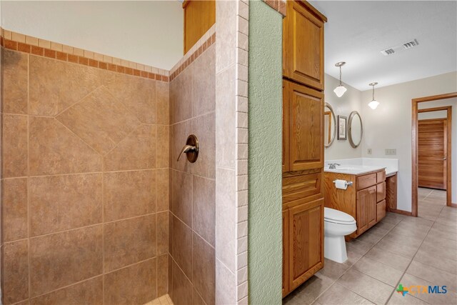 bathroom with toilet, vanity, tile patterned flooring, and a tile shower